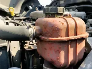 Rusty orange engine coolant reservoir with black hose in a vehicle engine bay