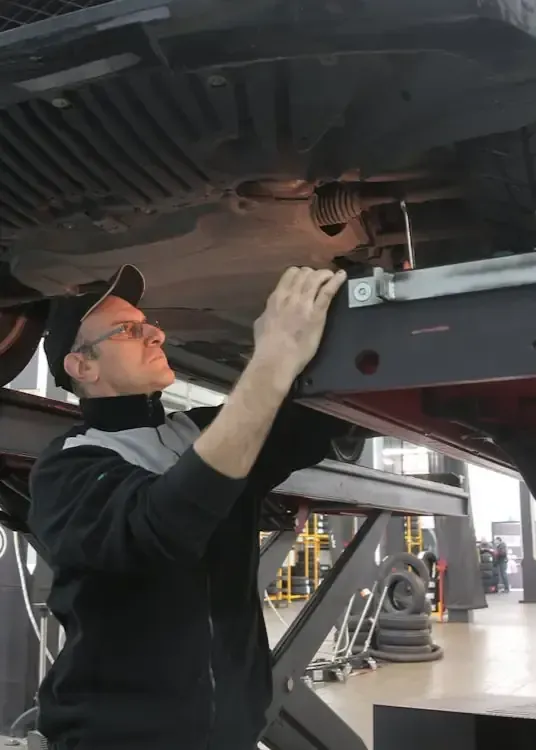 Mechanic inspecting the underside of a raised vehicle in an auto shop