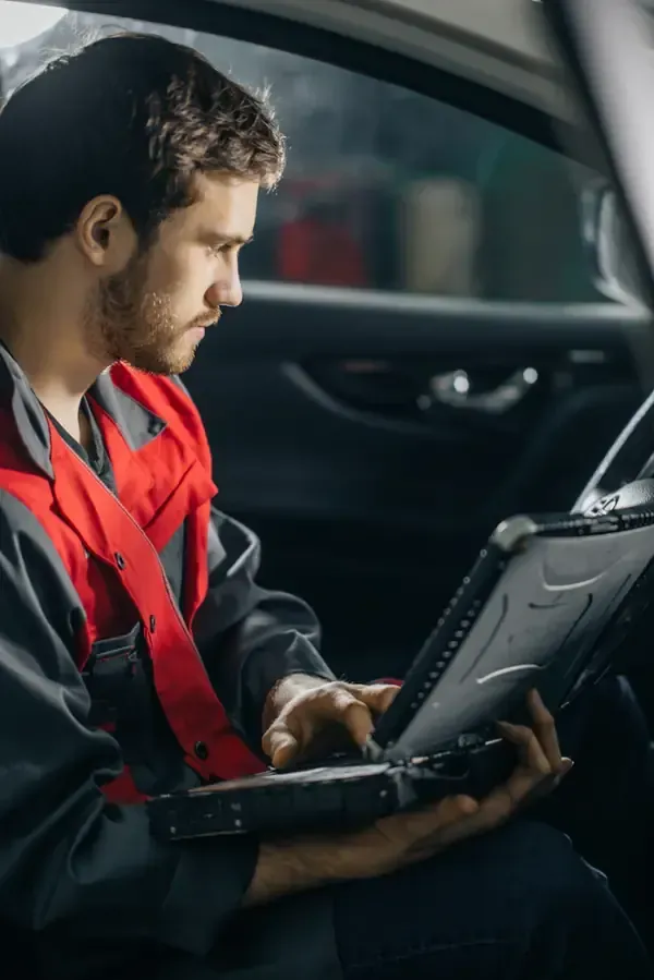 Mechanic in red-and-black uniform using a diagnostic tablet inside a car