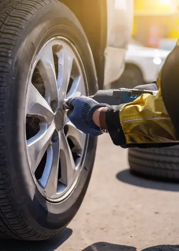 Gloved mechanic tightening a car wheel with a ratchet wrench outdoors, with another tire in the background