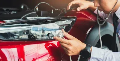 Mechanic using a tool to inspect a red car’s headlight in a garage