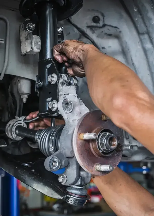 Mechanic working on a car suspension assembly with exposed wheel hub and brake components