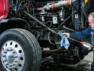 Mechanic cleaning a truck’s engine and wheel assembly with a cloth in a garage