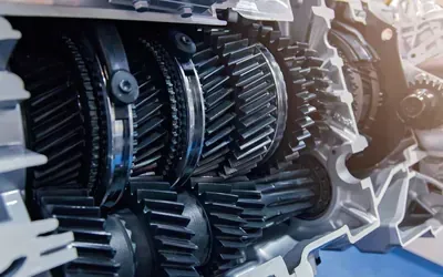 Close-up of interlocking metal gears and shafts inside a mechanical gearbox, lit by bright industrial light
