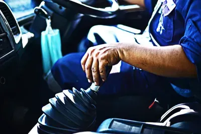 Person shifting gears in a car, hand on black gear stick inside a dark interior