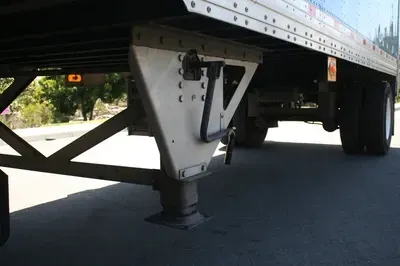 Underneath a semi-trailer, showing the landing gear and support frame on pavement.