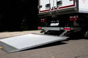 Truck with lowered white cargo ramp on pavement outside a building