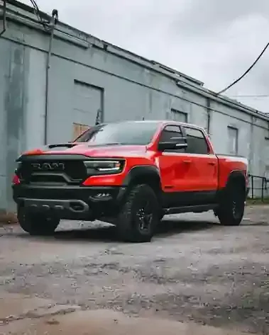 Red lifted pickup truck parked on cracked pavement beside a gray industrial building.