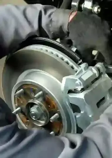 Gloved hands holding a car brake rotor and caliper in a repair shop