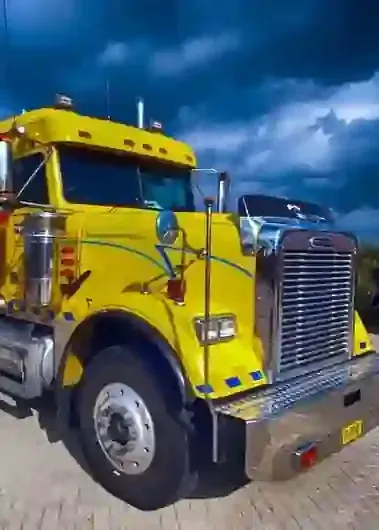 Bright yellow semi-truck cab parked outdoors under a dark cloudy sky