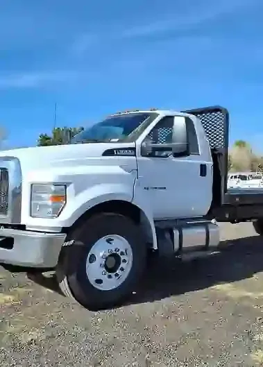 White flatbed truck parked on gravel under a clear blue sky