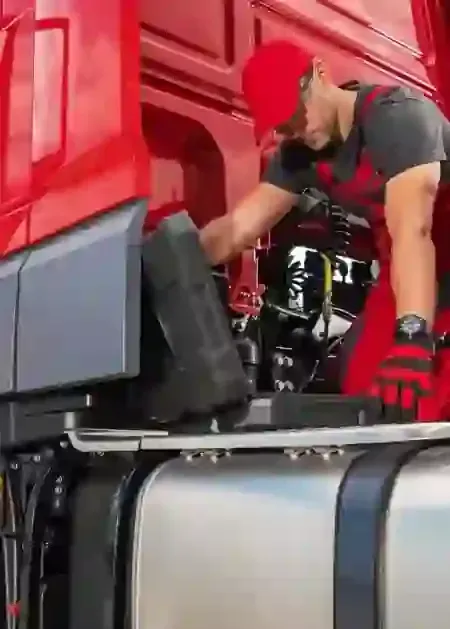 Mechanic in red cap working on a red truck engine in a garage