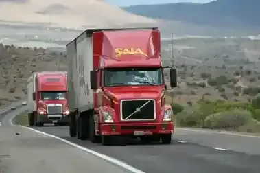 Two red Volvo trucks driving on a winding mountain road, one following closely behind the other.