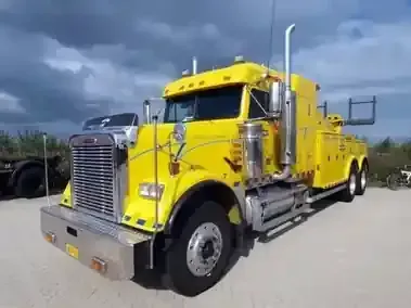 Yellow tow truck parked outdoors under cloudy sky