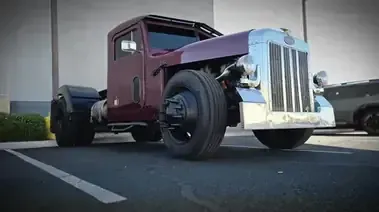 Maroon vintage hot rod truck parked in a lot, low-angle view with chrome grille and exposed engine.