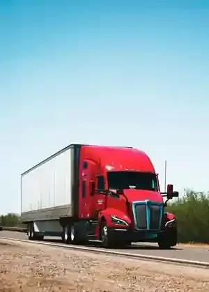 Red semi truck driving on a rural road under a clear blue sky