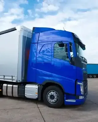 Blue semi-truck cab parked on pavement beside a white trailer at a loading area