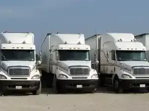 Three white semi trucks parked side by side on a lot under a clear sky