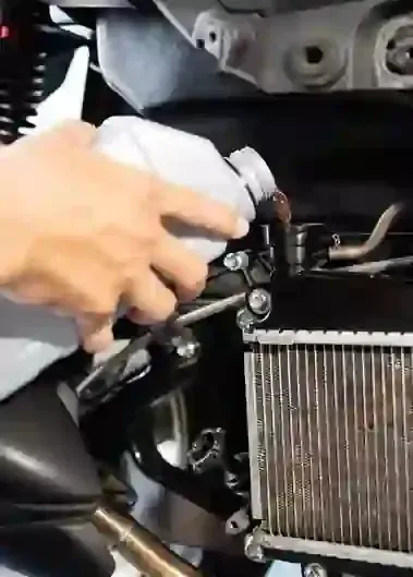 Hand spraying cleaner on an engine radiator and hoses inside a car's engine bay