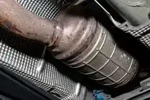 Close-up of a rusted car exhaust pipe and catalytic converter under the vehicle.