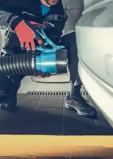 Person using a blue hose attachment to clean a car interior, wearing red gloves and black sneakers.