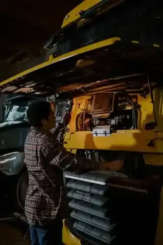 Person inspecting a yellow train carriage at night, lit by warm interior lights.