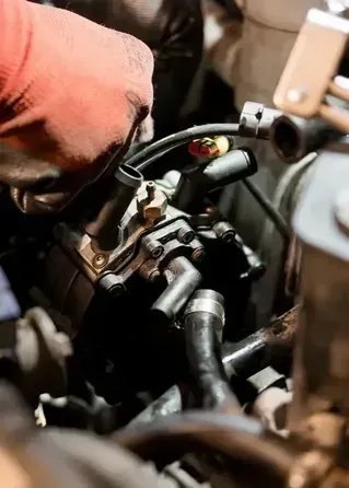 Gloved hand working on a black engine component with hoses and wiring close-up