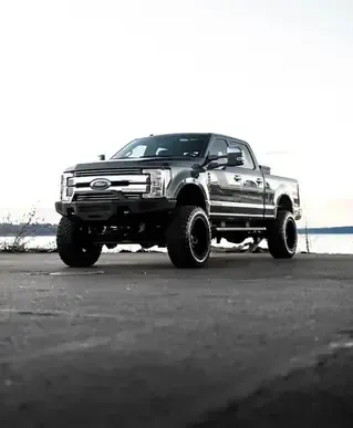 Black lifted pickup truck parked on pavement under a bright overcast sky