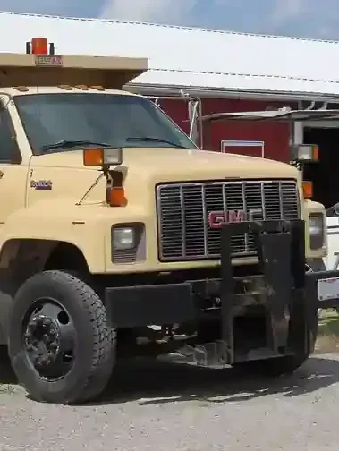 Beige utility truck parked in front of a building, with a black grille guard and side mirrors.