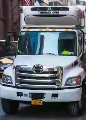 White refrigerated delivery truck facing forward on a city street, with a Thermo King unit on top.