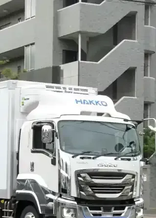 White HAKKO truck parked in front of a gray building with exterior stairs