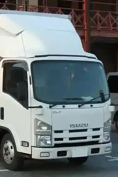 White Isuzu box truck parked on a street in front of a building