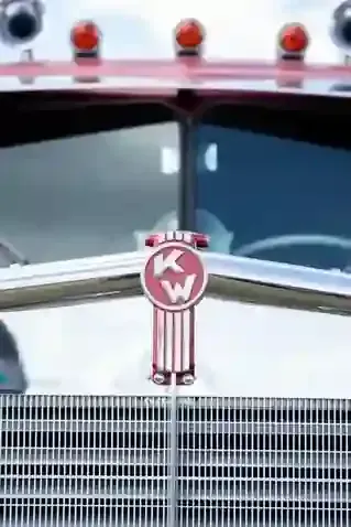 Close-up of a pink Kenworth truck grille and hood ornament with red marker lights above it