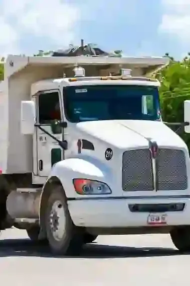 White garbage truck driving on a road outdoors