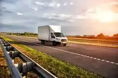 White delivery truck driving on a highway at sunset, with guardrail and open sky.