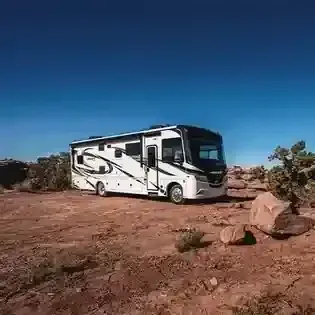 White RV parked on rocky desert ground under a clear blue sky.