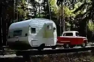 Red pickup truck towing a silver travel trailer through a wooded forest.