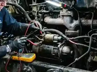 Mechanic working on a car engine with wires and a yellow multimeter in a cramped garage