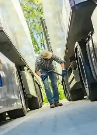 Person cleaning the floor between two buses, holding a mop in a narrow aisle