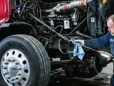 Mechanic cleaning a truck engine compartment with a blue cloth and spray tool