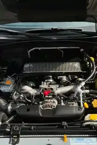 Car engine bay with exposed turbo piping and a bright red intake component, viewed from the front.