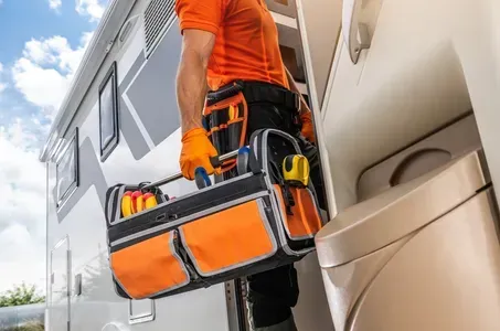 Technician in orange uniform carrying a tool bag beside a service van