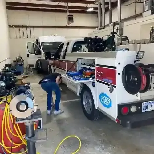 White service truck in a workshop while a worker in blue overalls cleans beside it.