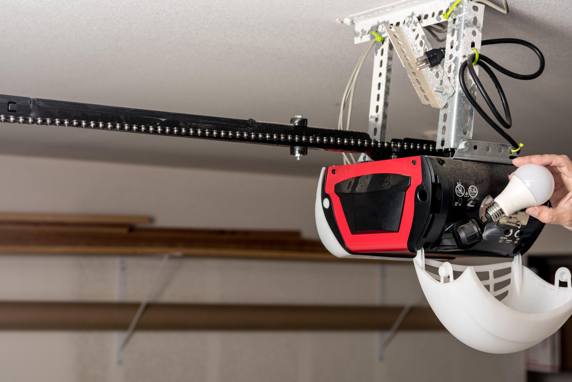 A person replacing a lightbulb in a garage door opener. The opener is mounted on a ceiling.