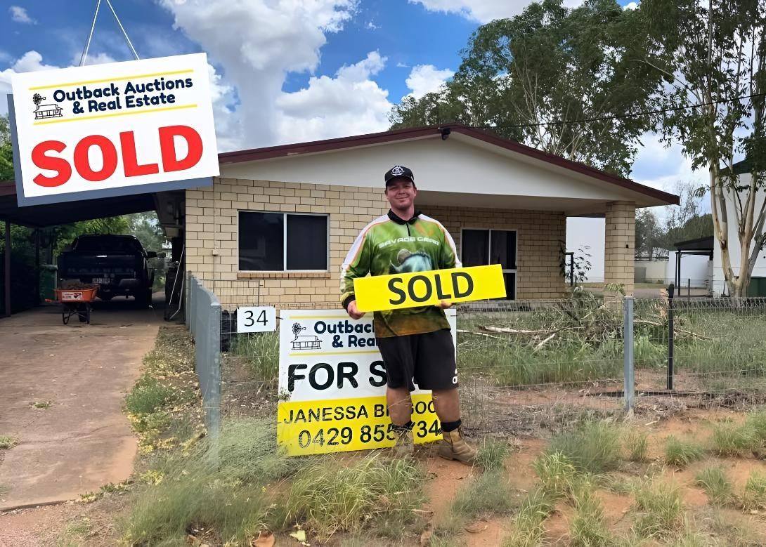A Man Is Holding A Sold Sign In Front Of A House โ Outback Auctions and Real Estate in Cloncurry, QLD