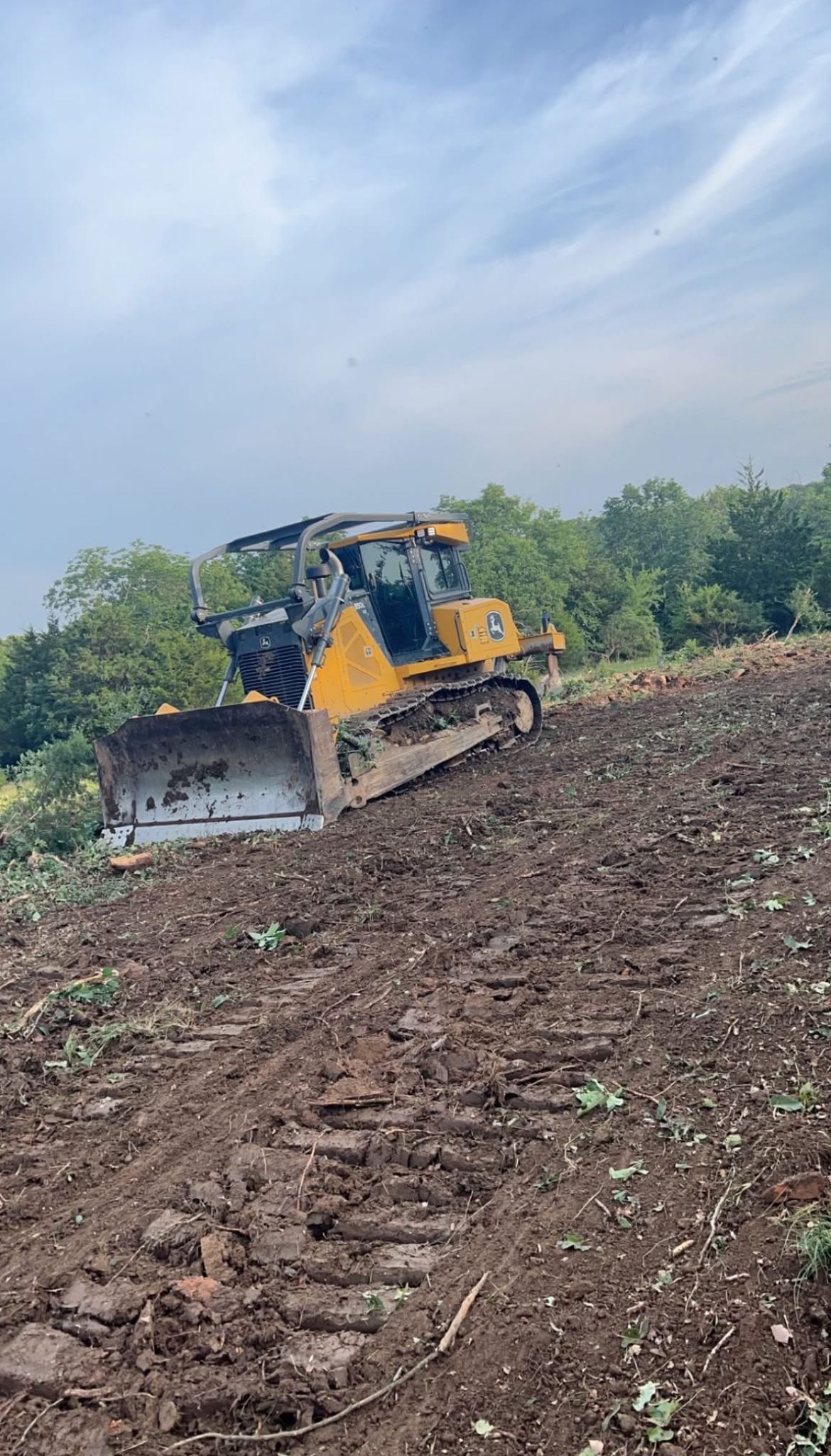 Yellow bulldozer clearing a muddy hillside under a cloudy sky