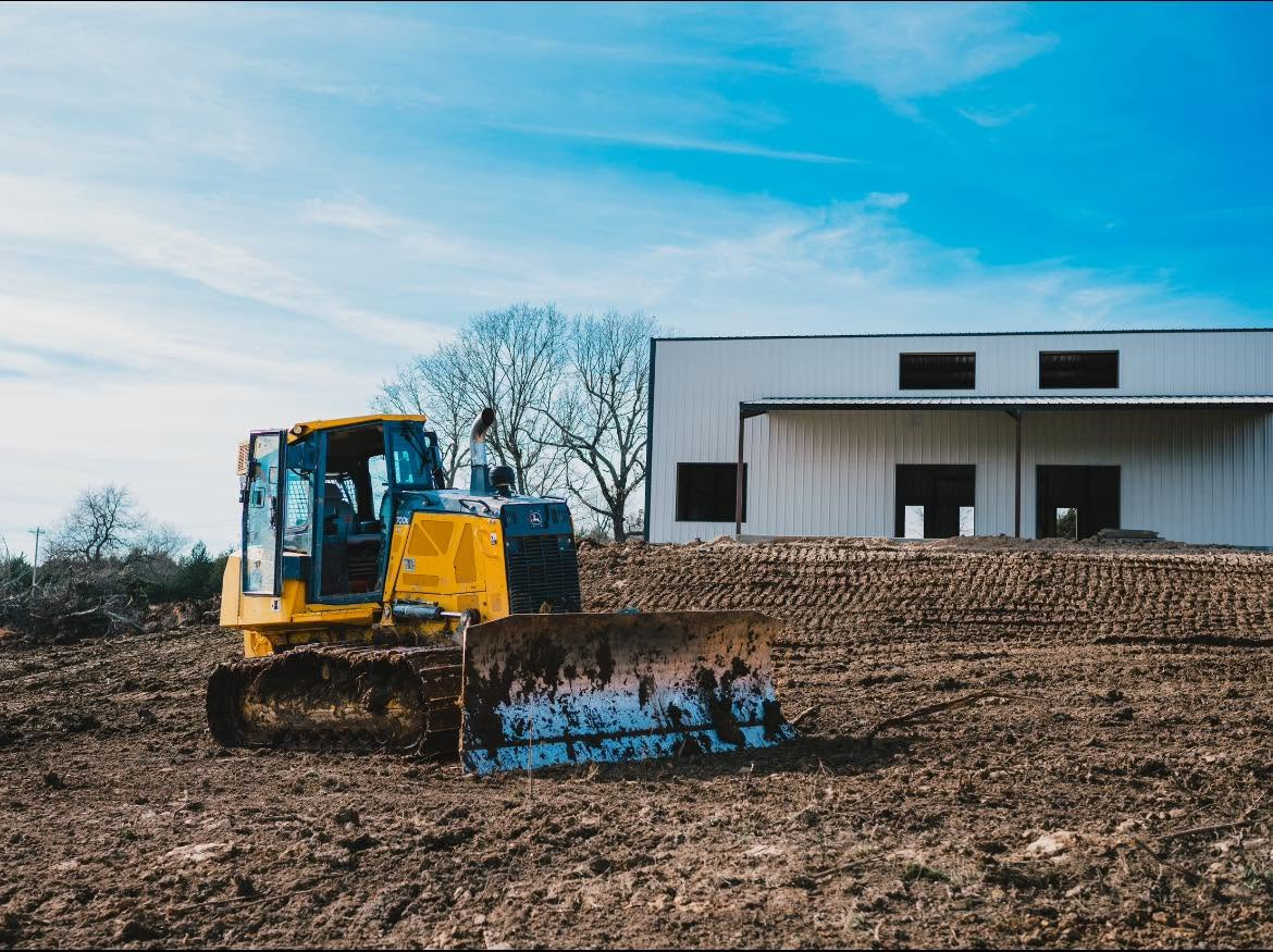 Yellow bulldozer on muddy construction site beside a white building under a blue sky