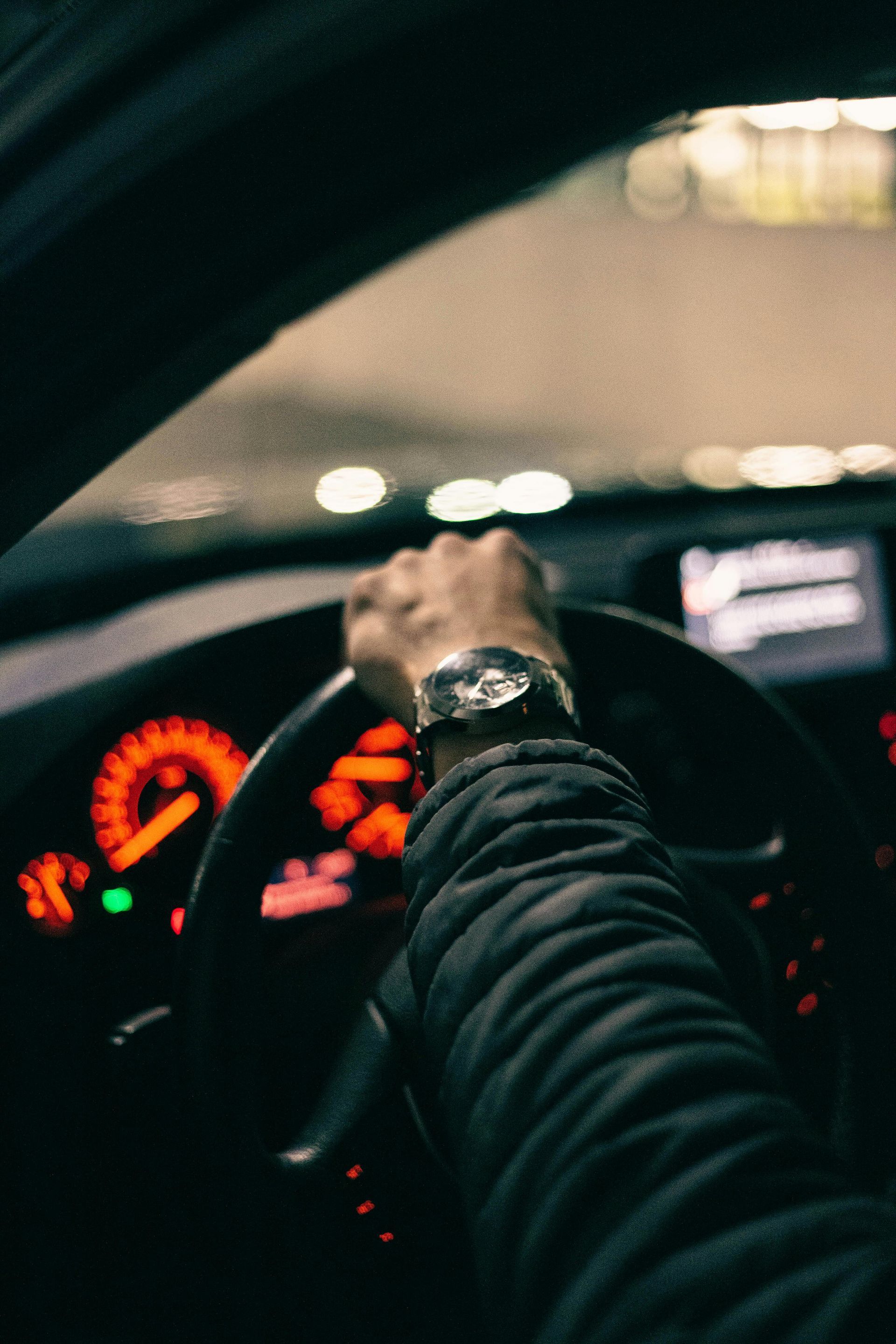 Driver’s hand on steering wheel at night, dashboard lights glowing orange inside a car
