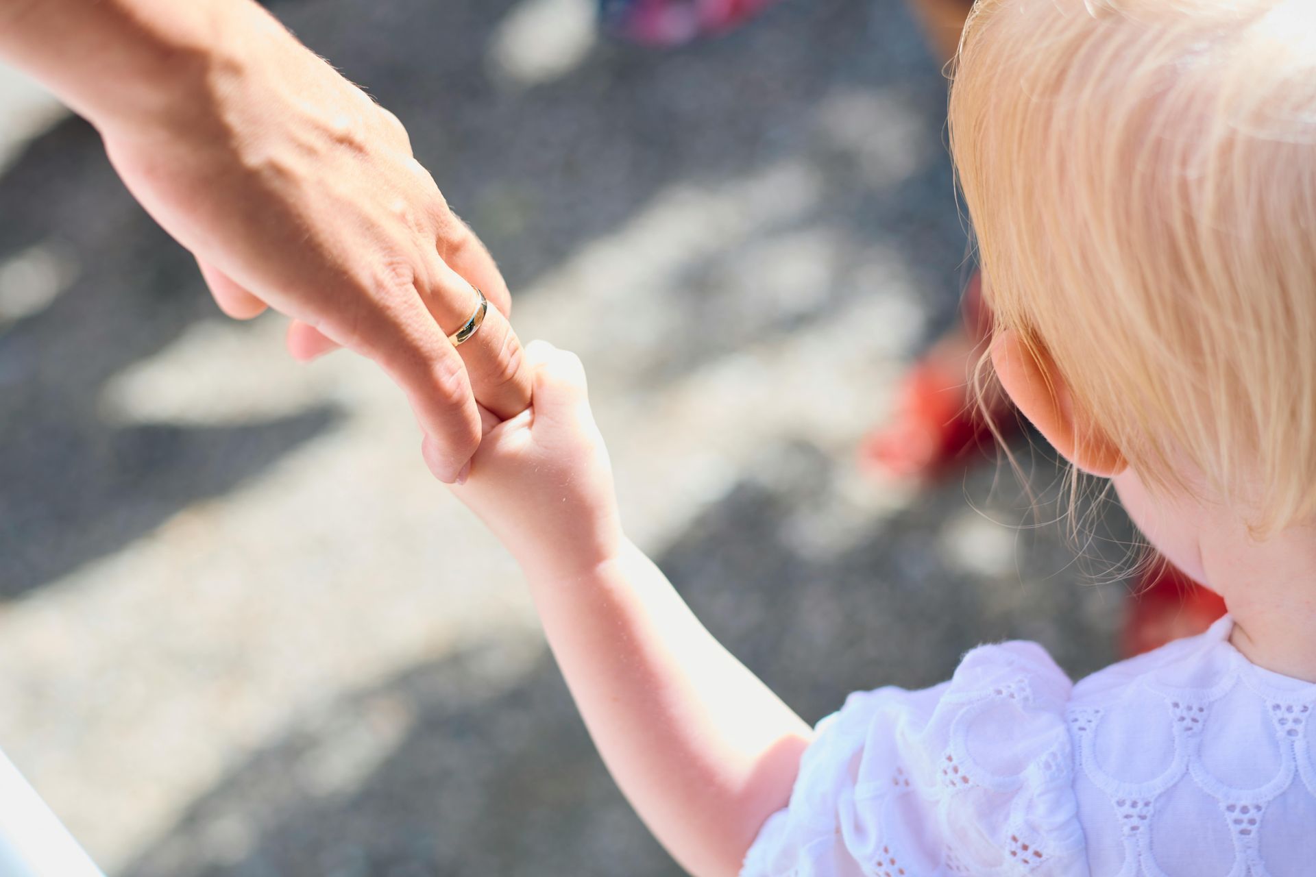 Adult hand holding a small child’s hand outdoors in bright sunlight