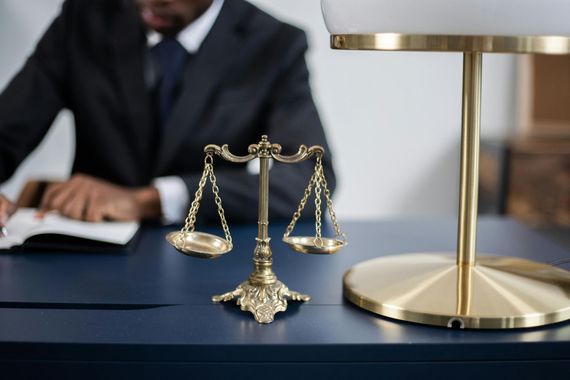 Miniature gold scales on a desk beside a lamp, with a blurred person writing in the background